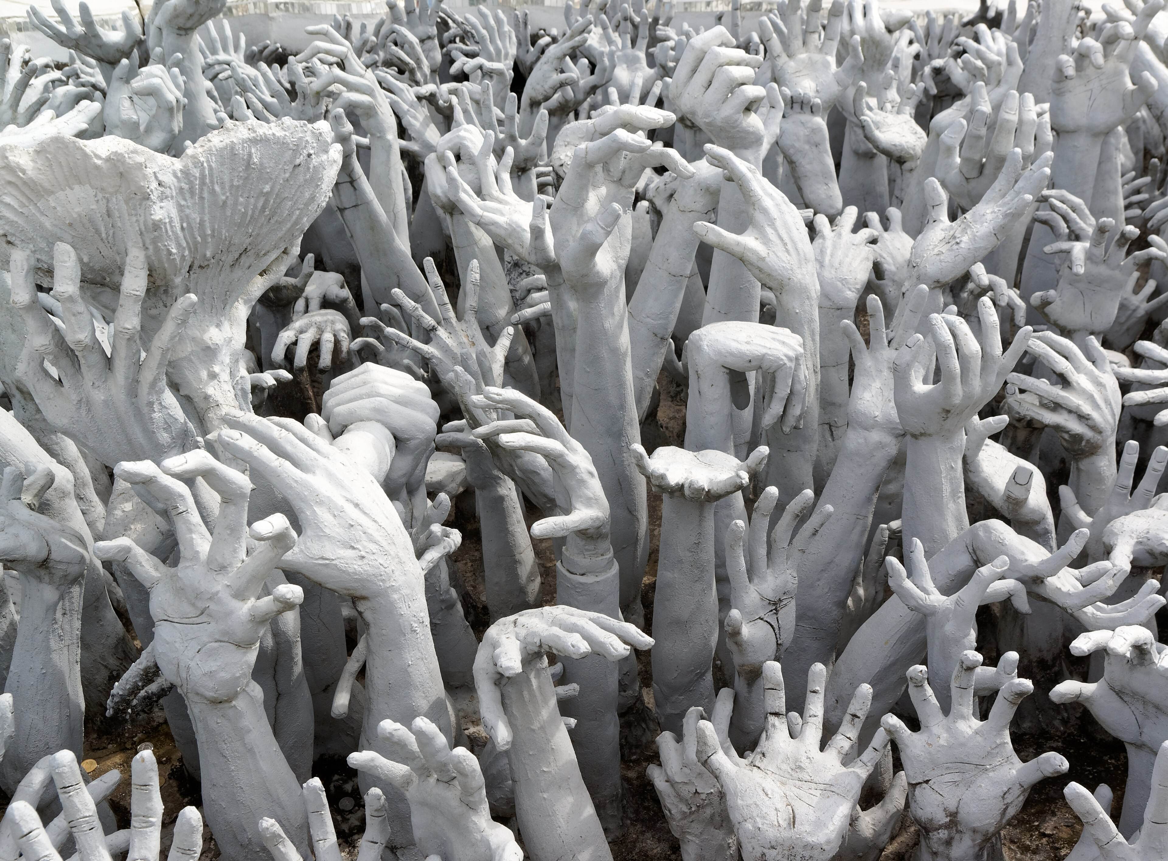 Hundreds of sculpted white hands reaching up beside the bridge at the White Temple